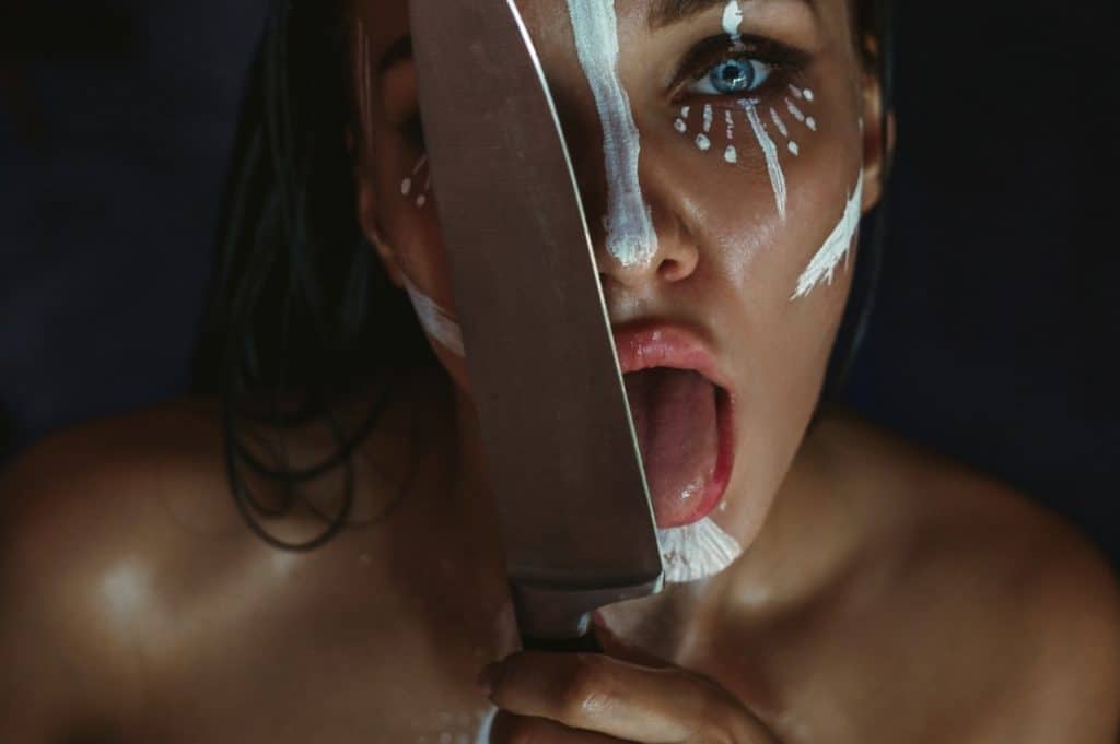 Young woman with artistic makeup licking kitchen knife