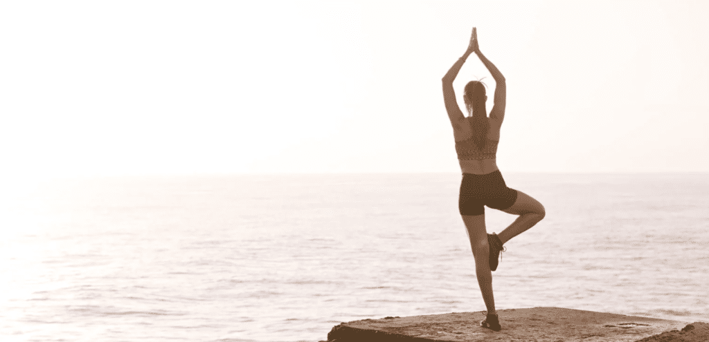 Woman Meditating On Rock Near Body Of Water