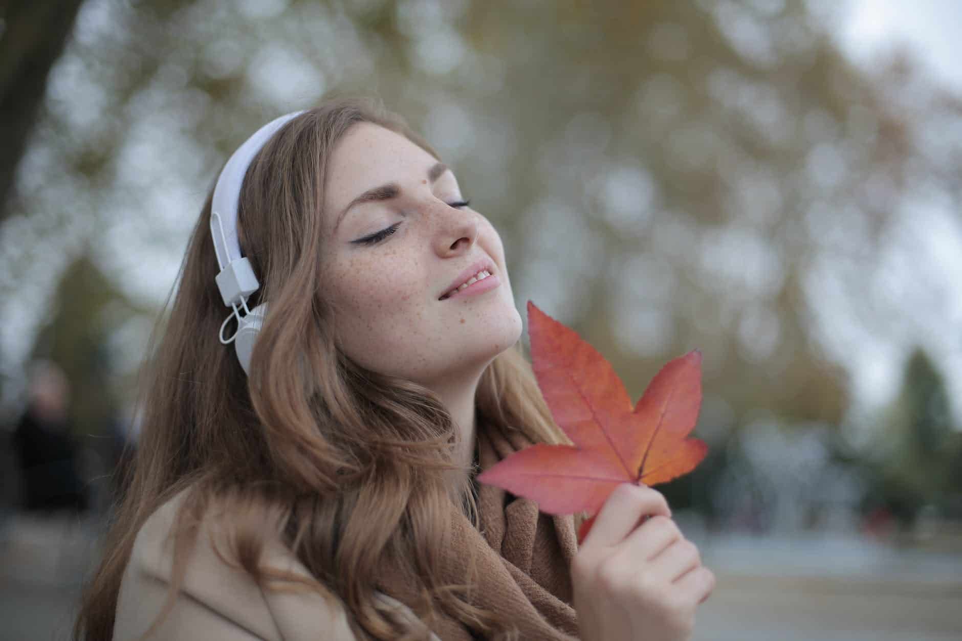 How To Budget For Holiday Spending In An Economic Downturn 5 young satisfied woman in headphones with fresh red leaf listening to music with pleasure while lounging in autumn park