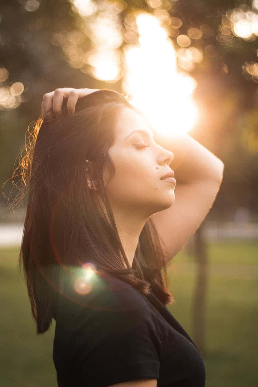 side view photo of woman with her eyes closed holding her her as sunlight shines on her face